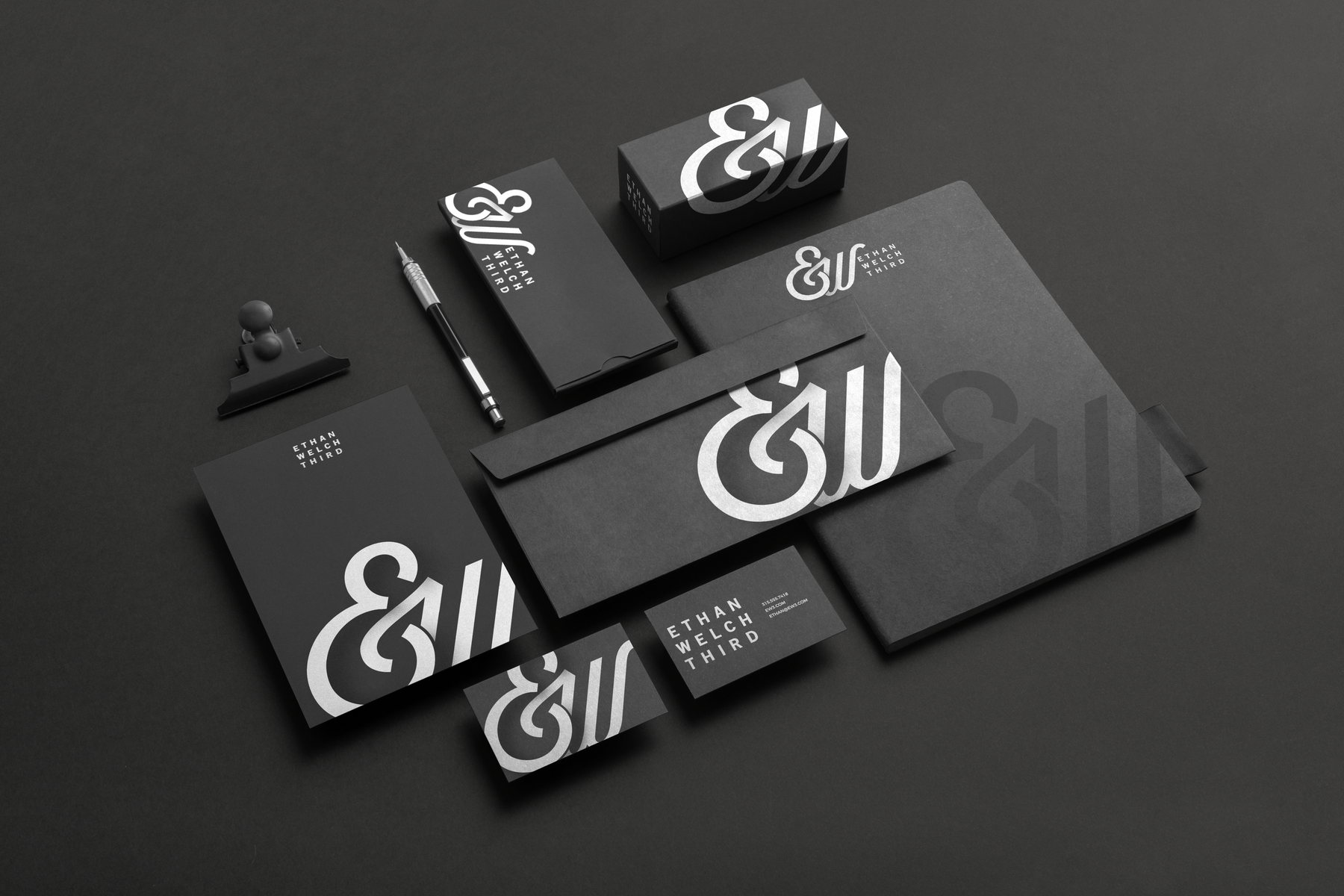 The black stationery suite: letterhead, envelopes, business cards, and a box, all carrying the white monogram